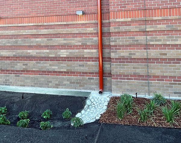 a downspout on a brick building with a drainage area below