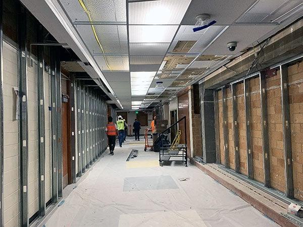 a hallway has metal walls supports over masonry blocks with construction workers walking down hall