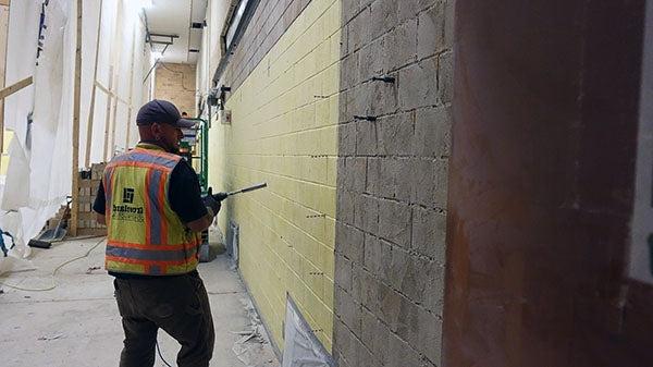 a worker has a large drill in front of a masonry wall in a space under construction