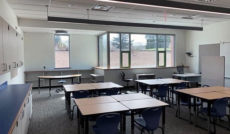 a room has groups of desks, windows and chairs