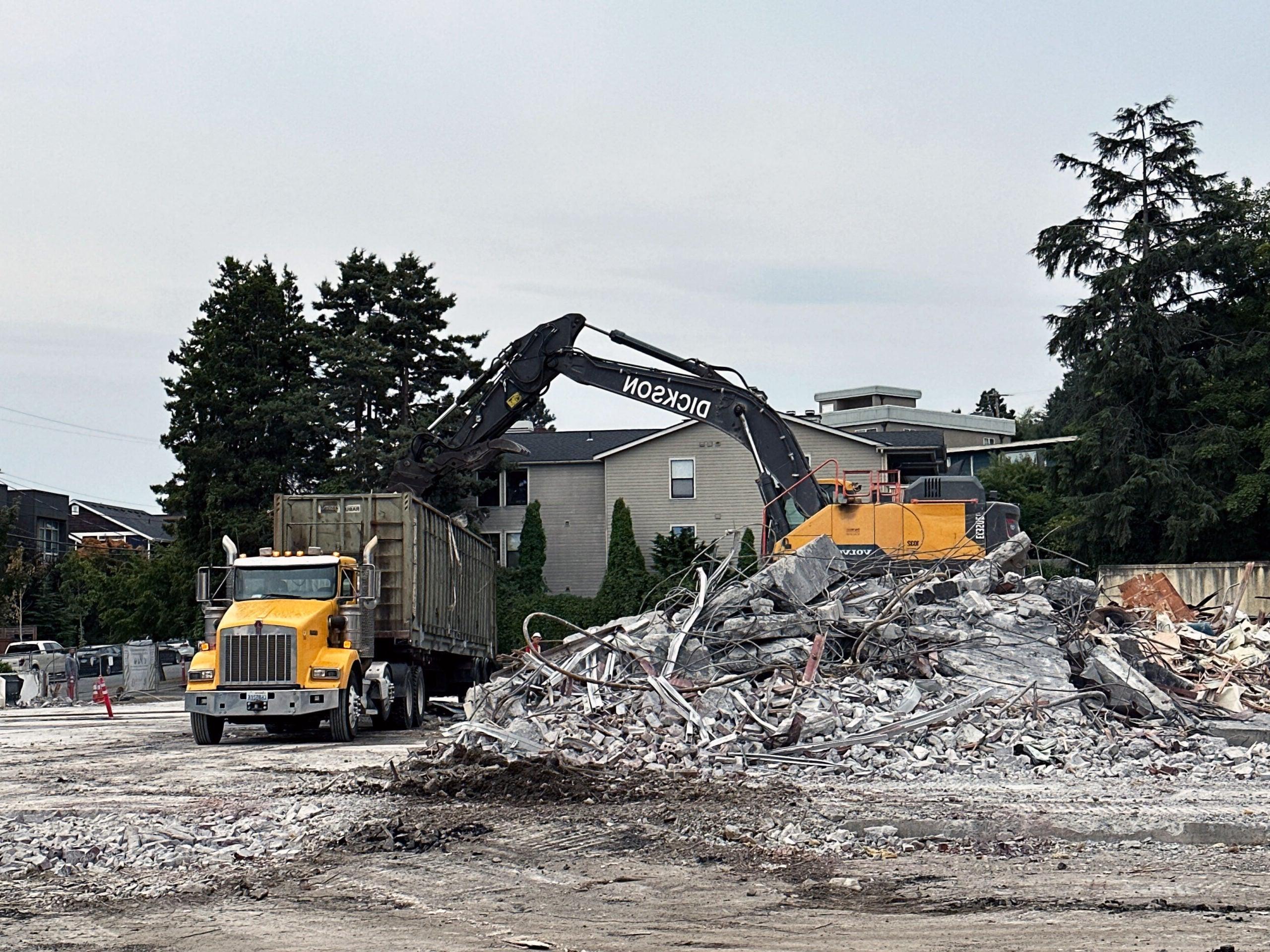 一辆挖掘机正在一堆混凝土瓦砾上向卡车上的一个集装箱排空