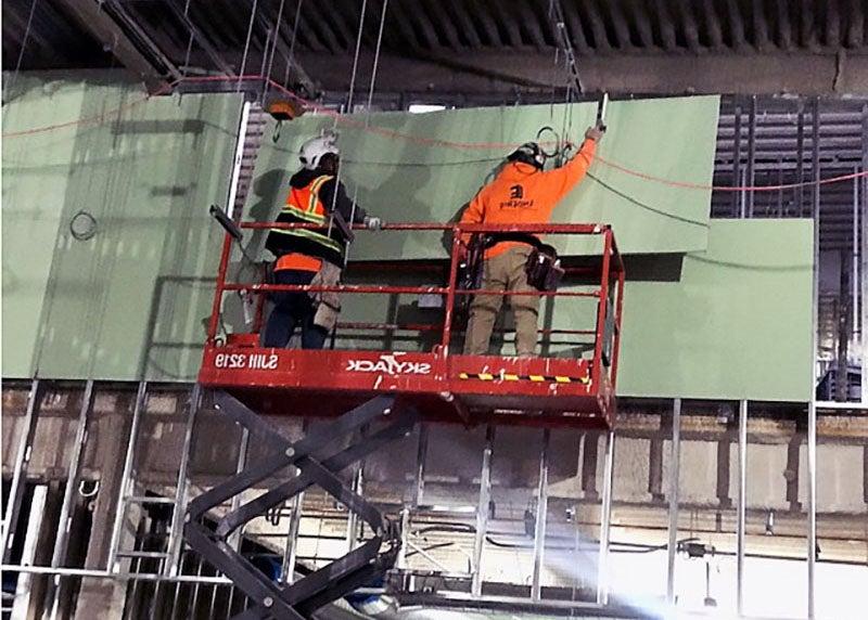 电梯上的两名工人正在把绿色墙板搬到室内建筑工地的钢架上