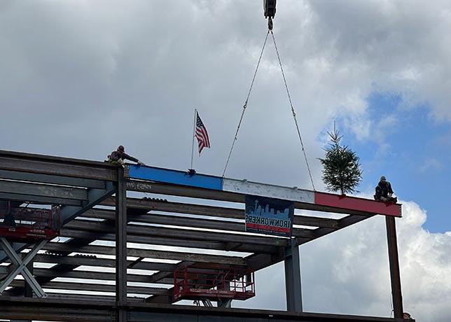 2个人在顶部的钢结构两侧各搭一个红色, white and blue beam that has an american flag and an evergreen tree on it